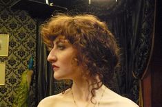 a woman with curly hair standing in front of a mirror wearing a necklace and dress