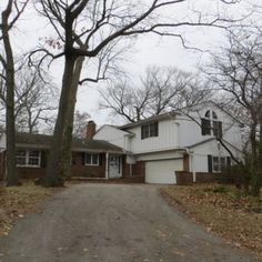 a white house sitting on the side of a road in front of trees and leaves