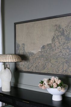 a vase with flowers sitting on a table next to a lamp and painting in the background