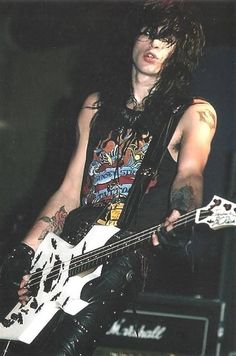 a man with long hair and piercings on his arm playing an electric bass guitar