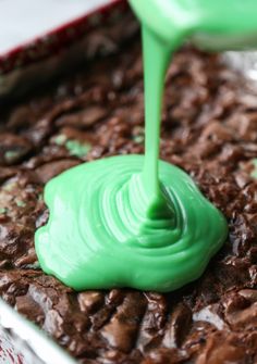 green icing being poured onto chocolate brownies