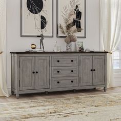 two paintings hang on the wall above a gray buffet cabinet with drawers and doors, in front of a beige area rug