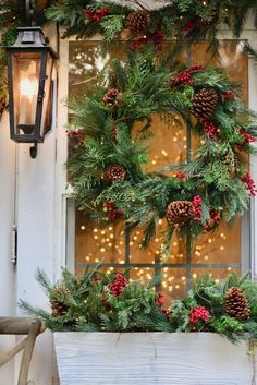 a christmas wreath is hung on the window sill with pine cones and red berries