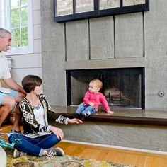 two adults and a baby sitting in front of a fireplace