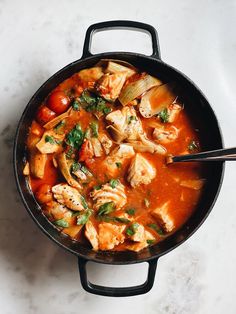 a skillet filled with chicken and vegetables on top of a white counter next to a wooden spoon