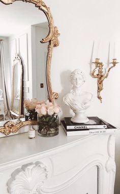 a white dresser topped with a vase filled with flowers next to a gold framed mirror