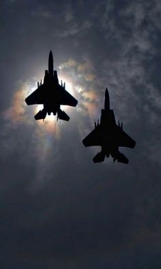 two fighter jets flying in the sky at night with the sun shining through clouds behind them