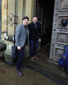 two men standing in front of an old building with pipes coming out of the door