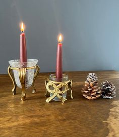 two lit candles sitting on top of a wooden table next to a glass bowl and pine cone