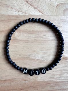 'Mito' stretch bracelet made with black glass matte beads and acrylic letters Personalized Black Minimalist Beaded Bracelets, Minimalist Personalized Black Beaded Bracelets, Personalized Minimalist Black Beaded Bracelets, Minimalist Adjustable Black Name Bracelet, Black Stretch Bracelet With Letter Beads And Round Beads, Black Stretch Bracelet With Letter Beads, Casual Black Stretch Bracelet With Letter Beads, Casual Black Beaded Name Bracelet, Black Beaded Name Bracelet With Round Beads