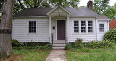 a small white house sitting next to a tree