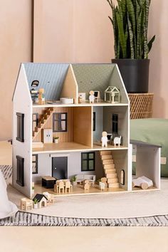 a doll house sitting on top of a table next to a pillow and potted plant