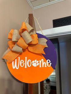 a welcome sign hanging from the side of a door with burlap and ribbon