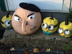 three pumpkins with faces painted on them sitting in front of a door and some plants