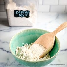 a wooden spoon in a green bowl filled with white flour next to a baking mix container