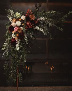 an arrangement of flowers and greenery is displayed on a stand in front of a fireplace