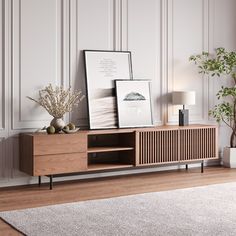 a wooden entertainment center with two pictures on top and a plant in the corner next to it