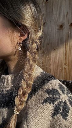 a woman with long hair wearing a sweater and earrings, standing in front of a wooden wall