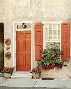 an orange door with red shutters and potted plants