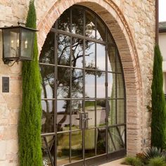 an arched window is shown in front of a stone building with potted plants and greenery