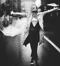 a woman holding an umbrella while walking down the street in the rain with her arms outstretched