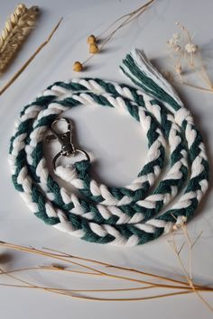 a white and green rope with a metal hook on it next to some dried plants