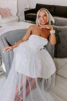 a woman sitting in a chair wearing a white dress and holding her hand on her cheek