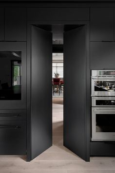 an open door leading into a kitchen with black cabinets and stainless steel appliances in it