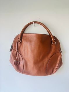 Salvatore Ferragamo Large Brown Leather Hand Bag in excellent condition. Silver hardware with signature fabric interior. Zipper closure with added snap lock. Such a beautifully constructed piece. Will be a great addition to any wardrobe. Leather clean only. Approx. measurements: Width: 13" Length: 17" Modern Cognac Satchel With Palladium Hardware, Brown Satchel With Silver-tone Hardware Top Handle, Brown Satchel With Silver-tone Hardware, Brown Top Handle Satchel With Silver-tone Hardware, Cognac Bag With Silver-tone Hardware And Top Handle, Classic Brown Satchel With Round Handle, Office Satchel In Brown With Silver-tone Hardware, Brown Office Satchel With Silver-tone Hardware, Cognac Leather Shoulder Bag With Silver-tone Hardware