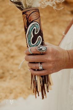 a person holding a wedding bouquet with feathers on it's arm and ring in their hand