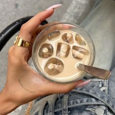 a woman holding a glass filled with liquid and ice cubes on top of it