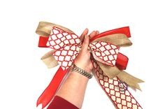 a woman's hand holding two red and beige bows on her left wrist, against a white background