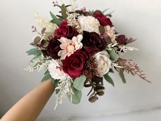 a bridal bouquet with red, white and pink flowers is held by someone's hand