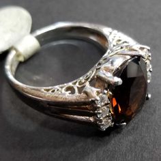 Vintage sterling silver ring with. Center CZ is deep brown (Smoky Quartz color) measuring 11x10mm, with three clear CZs on each side in an engagement ring style. The Euro band has intricate cutout scrollwork with beautiful craftsmanship. The ring shank is 2.5mm wide at the back. If you love finding unique treasures, then a vintage ring may be just the thing to add to your collection. Our family acquired this ring around 2000, as part of a large jewelry collection. It's in great condition, unworn Oval Brown Jewelry For Anniversary, Brown Oval Jewelry For Anniversary, Formal Oval Topaz Ring With Stone Setting, Brown Rings With Prong Setting For Anniversary, Oval Three Stone Topaz Ring For Formal Occasions, Brown Gemstone Rings For Anniversary, Formal Oval Diamond Ring With Stone Setting, Brown Round Rings For Anniversary, Brown Prong Set Ring For Anniversary