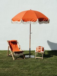 an orange and white umbrella sitting next to two lawn chairs on top of a grass covered field