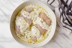 a bowl filled with meat and cheese on top of a white marble counter next to a striped towel