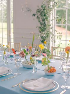 a table set with plates, glasses and flowers in vases on top of it