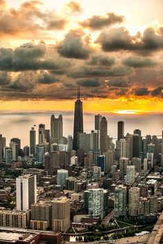 an aerial view of a large city with tall buildings and clouds in the sky at sunset