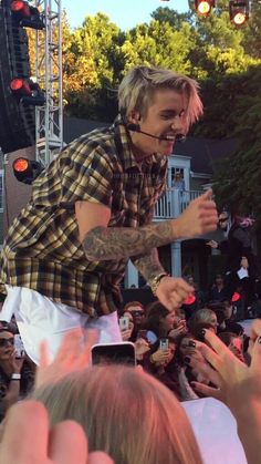 a man in plaid shirt and white pants standing on stage with his hands up to the crowd