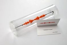 an orange string in a glass tube with a note inside it and a card attached to the end