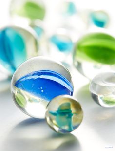 several glass marbles with different colors and shapes on a white surface, including green leaves