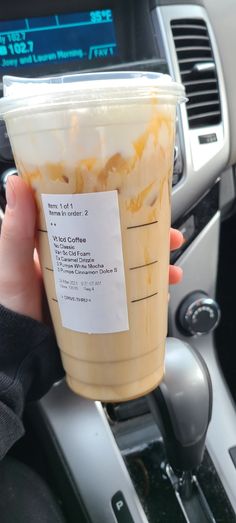 a person holding up a plastic cup with food inside of it on the dashboard of a car