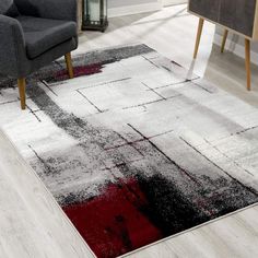 an area rug with red and black designs on it in a living room next to a gray chair