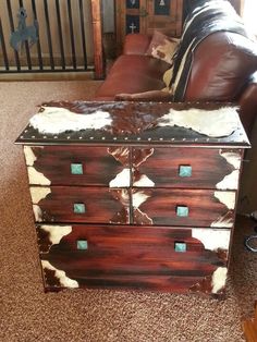 a brown leather couch sitting next to a wooden chest on top of a carpeted floor