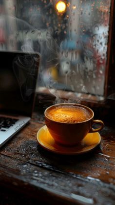 a cup of coffee sitting on top of a saucer next to a laptop computer