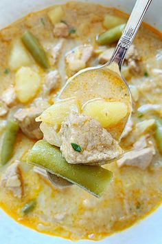 a spoon full of soup with meat, potatoes and green beans on it in a white bowl