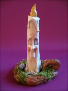 a small white candle with a smiling face on top of mossy branches and a purple background