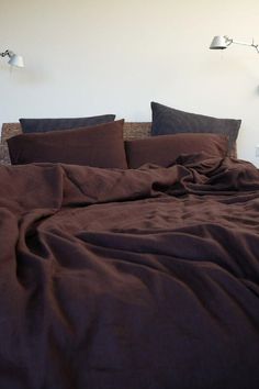 an unmade bed with two lamps on either side and dark brown sheets in the foreground