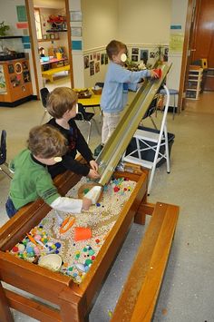 three children are playing with toys in a room filled with wooden tables and desks