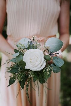 a bridesmaid holding a bouquet of white flowers and greenery in her hands